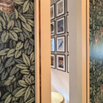 A view through a doorway showcasing the contrast between bold Fornasetti owl wallpaper and a minimalist gallery wall of vintage New Yorker covers