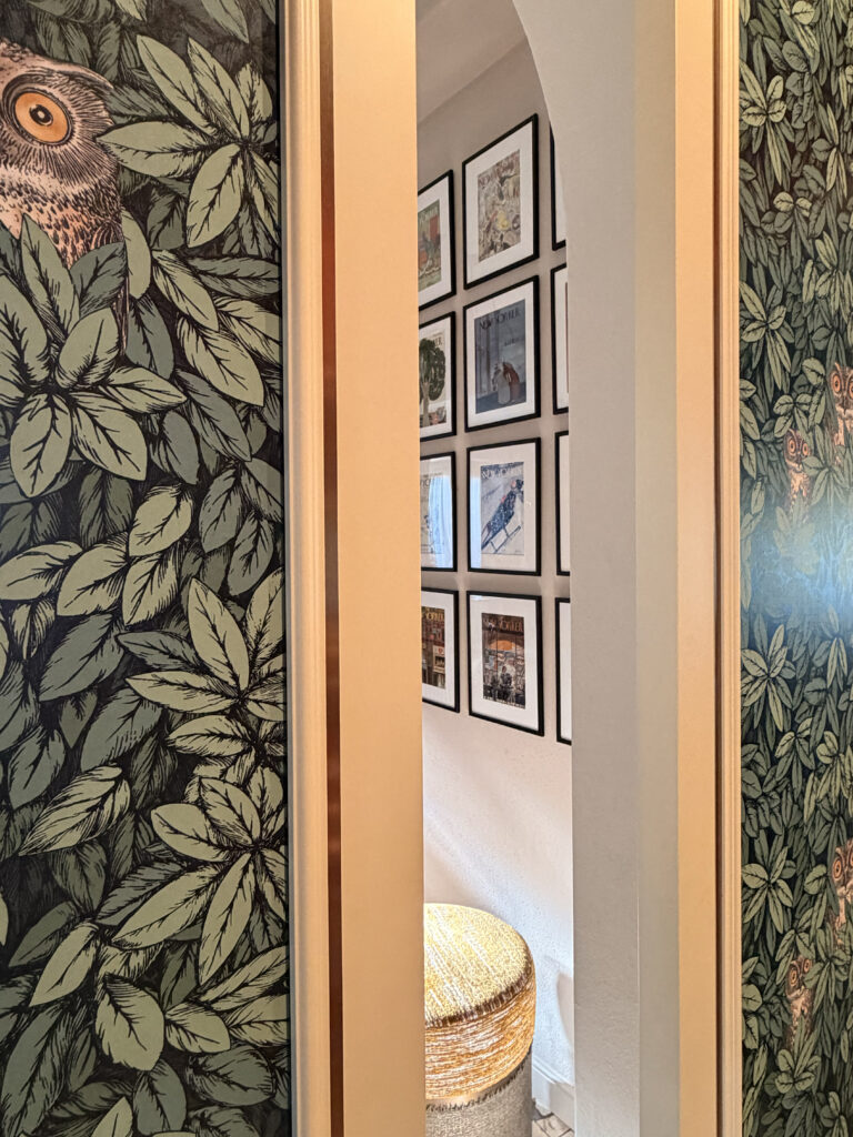 A view through a doorway showcasing the contrast between bold Fornasetti owl wallpaper and a minimalist gallery wall of vintage New Yorker covers