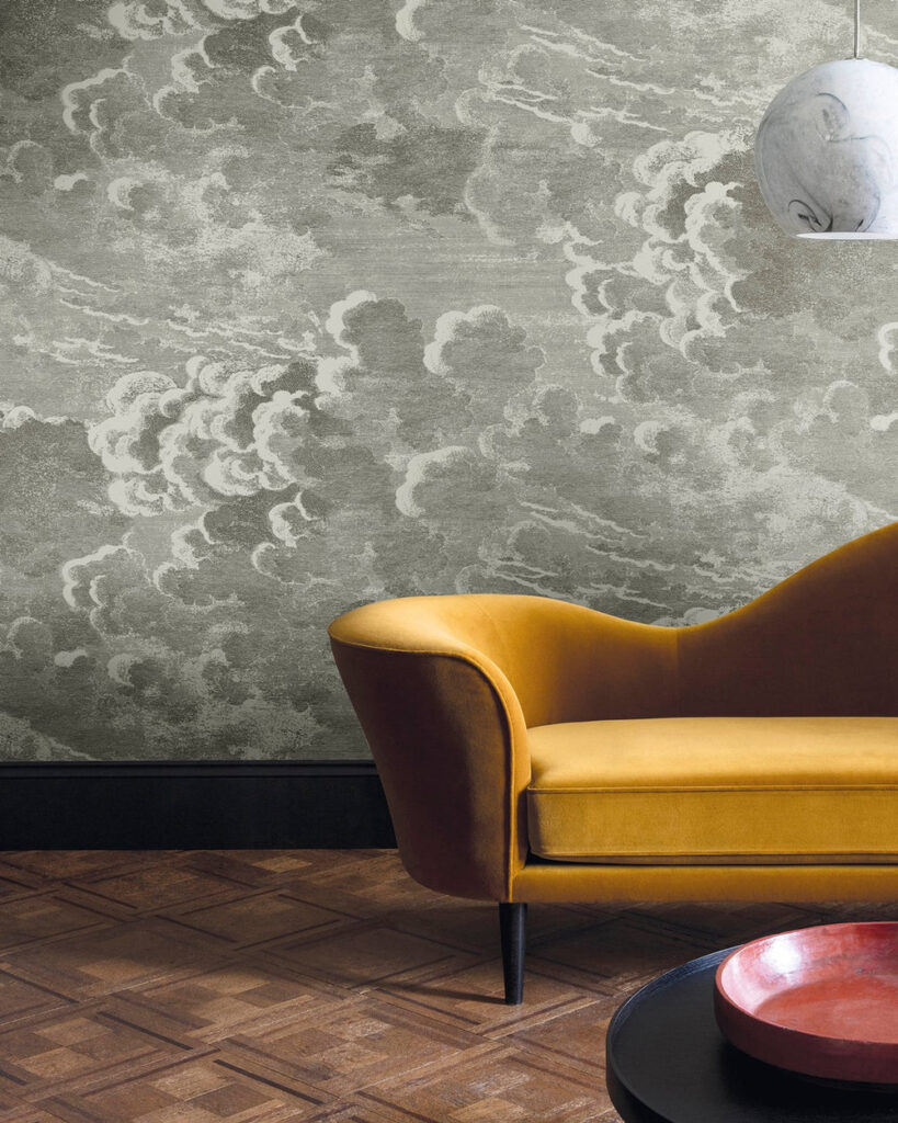 A statement wall using Fornasetti cloud-patterned wallpaper to add depth and texture to a room with high-contrast furniture and traditional wood floors