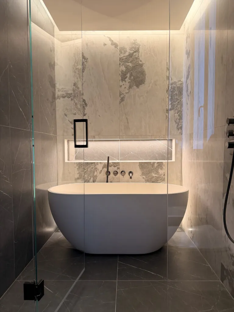Turnkey execution of a luxury marble wet room with freestanding oval bath and recessed LED architectural lighting by Paolo Rota Interiors