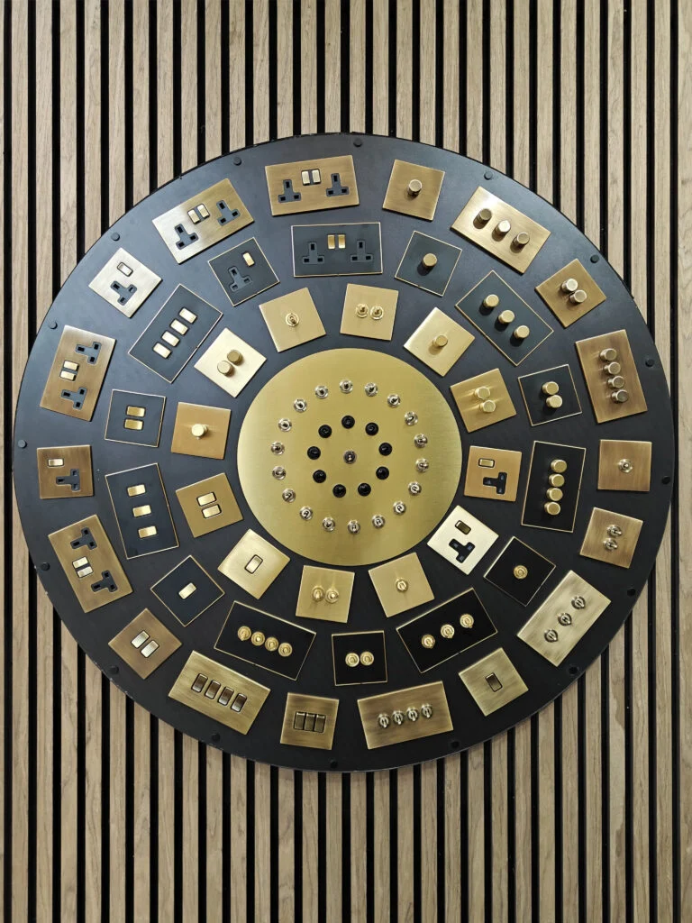 Radial architectural hardware display featuring burnished brass switches, toggles, and dimmers at Decorex London