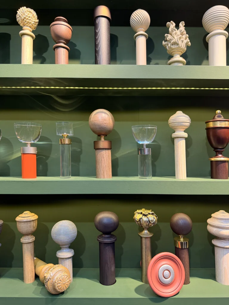Curated wall display of luxury drapery finials in carved wood, optical glass, and gilded brass at Decorex London