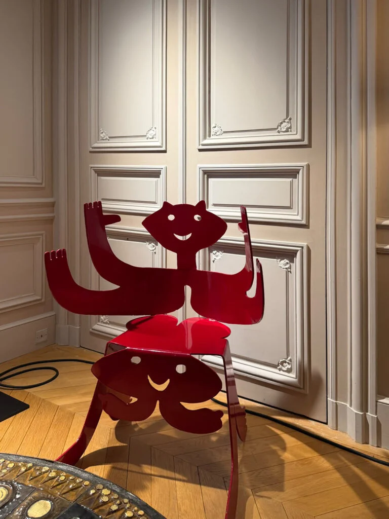 High-gloss scarlet red sculptural chair with anthropomorphic silhouette placed against classic French boiserie molding at Design Miami Paris