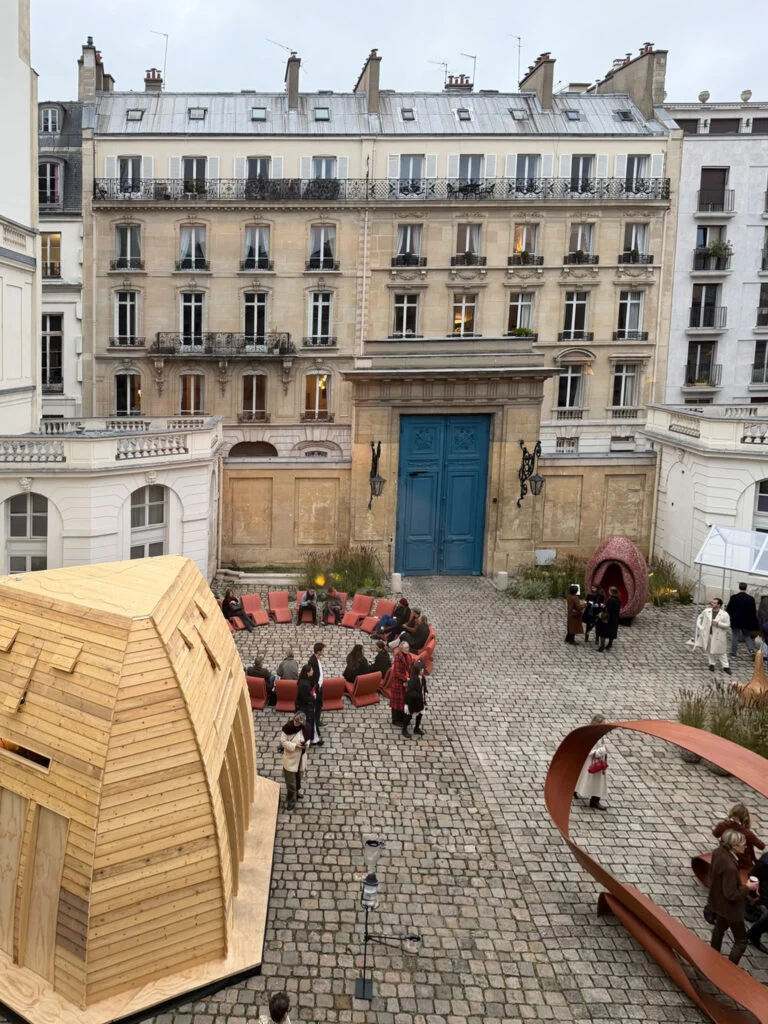 Courtyard of L'Hotel de Maisons featuring the faceted timber architectural pavilion, circular lounge seating, and corten steel sculpture