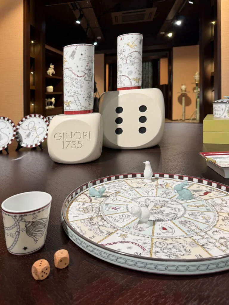 Ginori 1735 Fortunae porcelain tableware display featuring oversized decorative dice, astrological game board platter, and animal game markers