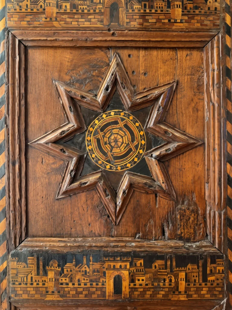 Main entrance door featuring a prominent wooden star intarsia inlay at Palazzo Ducale in Gubbio